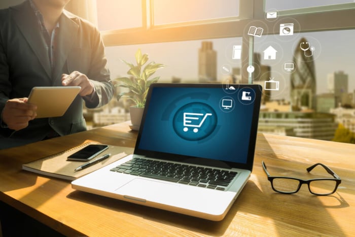 laptop em mesa de escritorio com simbolo de carrinho de compras em tela simbolizando o e- commerce