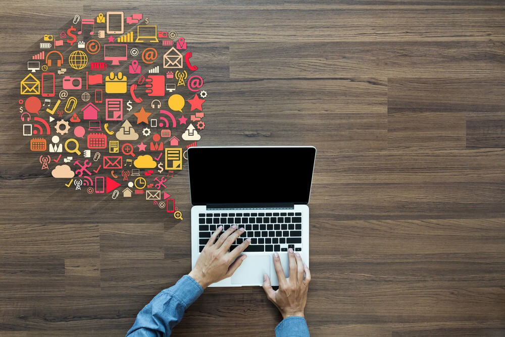 maos masculinas em teclado de laptop com ilustraçao de objetos de produçao ao lado