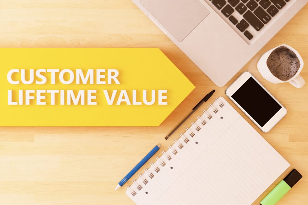 mesa executiva com materiais de escritorio, smartphone e laptop com a frase costomer lifetime value