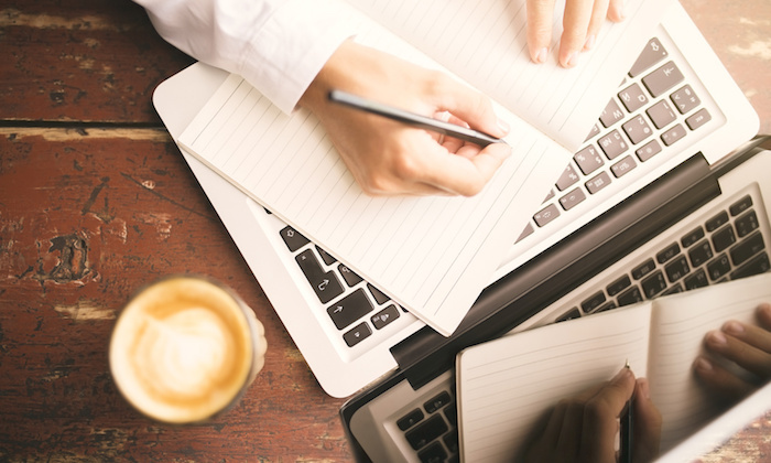 Man hands writing in the diary, coffee mug and laptop on wooden table